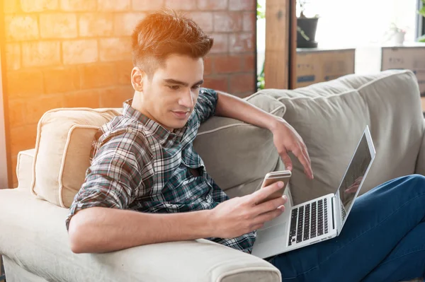 Zakenman met behulp van smartphone en laptop schrijven op sofa in koffie — Stockfoto