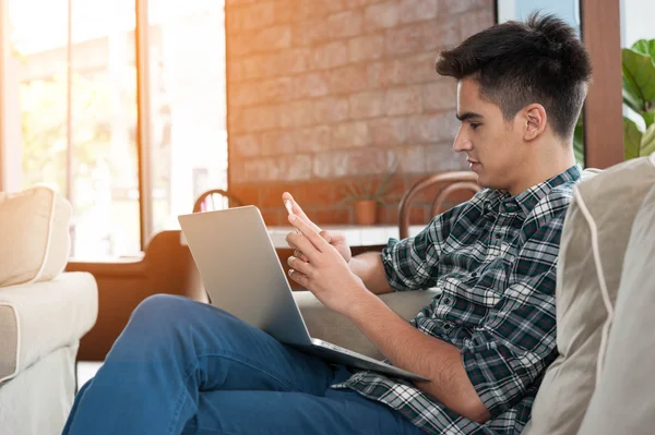 Zakenman met behulp van smartphone en laptop schrijven op sofa in koffie — Stockfoto