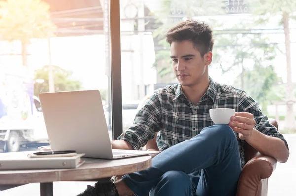 Uomo che beve caffè con computer portatile su tavolo di legno in caffetteria — Foto Stock