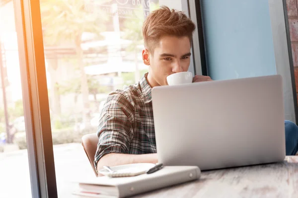 Uomo che beve caffè con computer portatile su tavolo di legno in caffetteria — Foto Stock