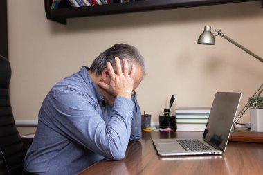 Kıdemli adam bilgisayar kullanmayı öğrendi. Cam ve mavi tişörtlü yaşlı adam ev ofisinde çalışmak için dizüstü bilgisayar kullanıyor.