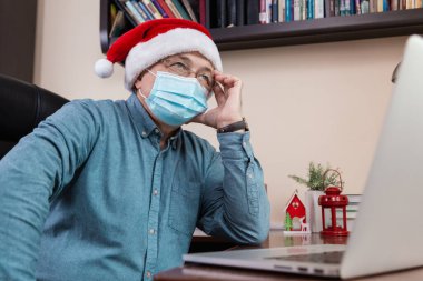 Noel online tebrik fikri. Noel Baba şapkalı son sınıf öğrencisi, bilgisayar kullanarak arkadaşları ve çocukları arıyor. Oda şenlikle dekore edildi. Coronavirus sırasında Noel.