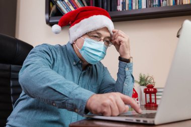 İnternette Noel kutlamaları zor oluyor. Noel Baba şapkalı son sınıf öğrencisi, bilgisayar kullanarak arkadaşları ve çocukları arıyor. Oda şenlikle dekore edildi. Coronavirus sırasında Noel.