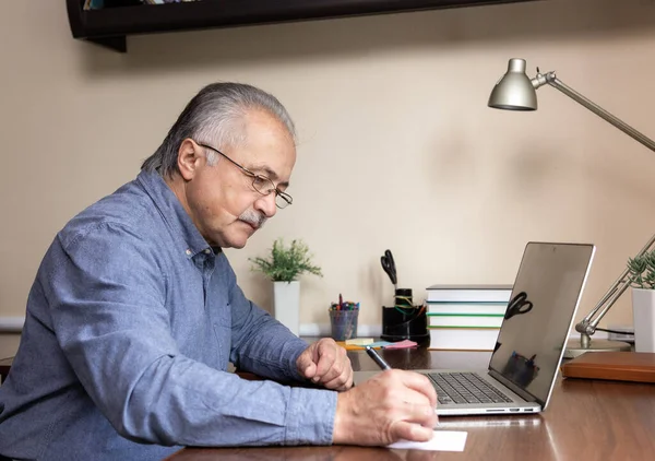 Senior man learn to use computer. Old man in glass and blue shirt using a laptop computer for online studying at home office