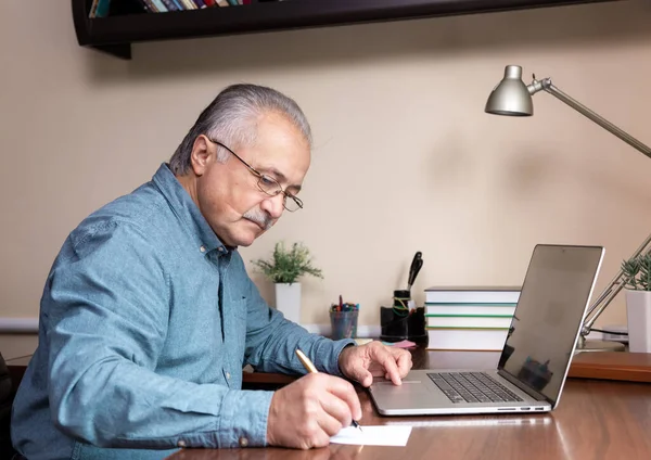 Senior man learn to use computer. Old man in glass and blue shirt using a laptop computer for online studying at home office