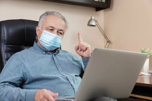 senior man in face mask working or communicate on laptop at home. study, training, work, communication, entertainment, leisure during the coronavirus period.