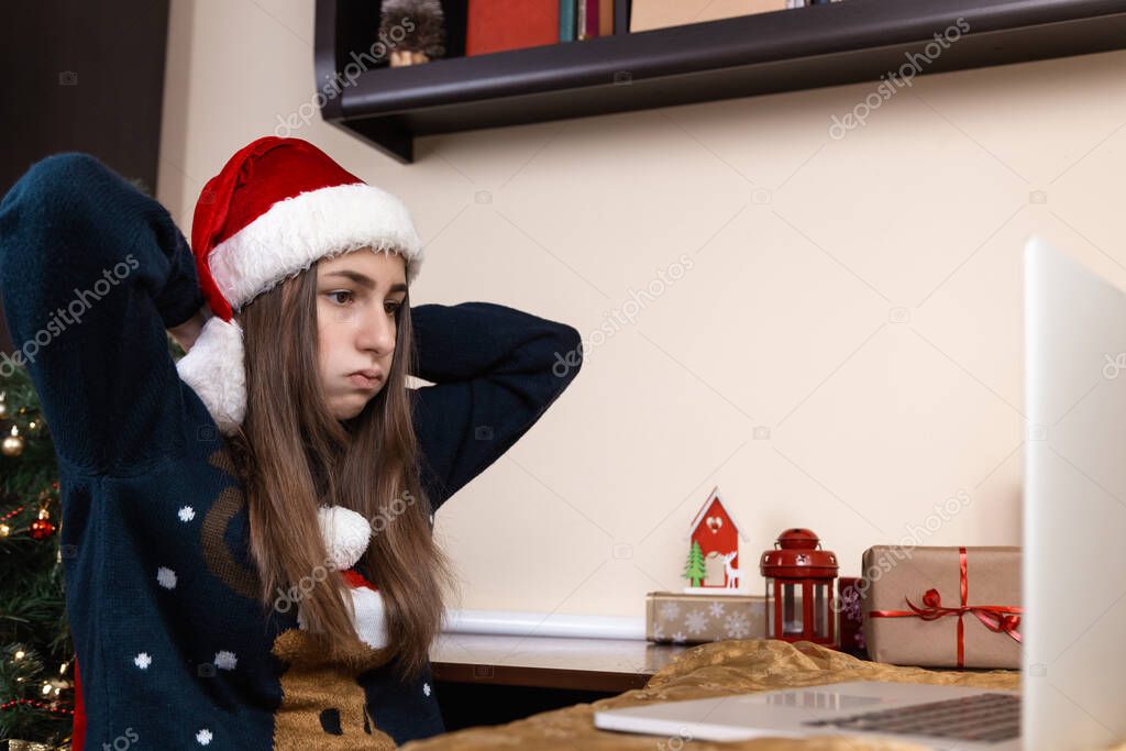Christmas online congratulation. girl in santa claus hat talks using laptop for video call friends and parents. The room is festively decorated. Christmas during coronavirus. fatigue