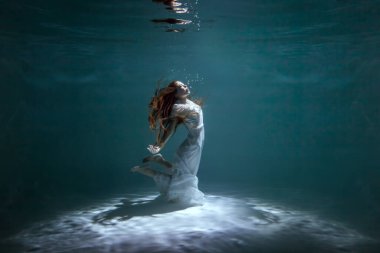 Beyaz elbiseli bir kadın su altında dans ederken gösteri yapıyor..