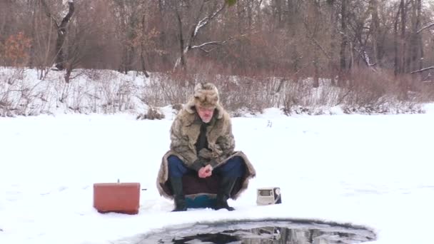 Ηλικιωμένος Κάθεται Ένα Καλάμι Ψαρέματος Στην Τρύπα Πάγου Στη Λίμνη — Αρχείο Βίντεο