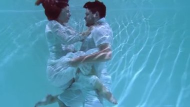 Bir erkek ve bir kadın suyun altında dans ediyorlar. İnsanlar kıyafetleriyle suya dalıp birbirlerine sarılıyorlar..