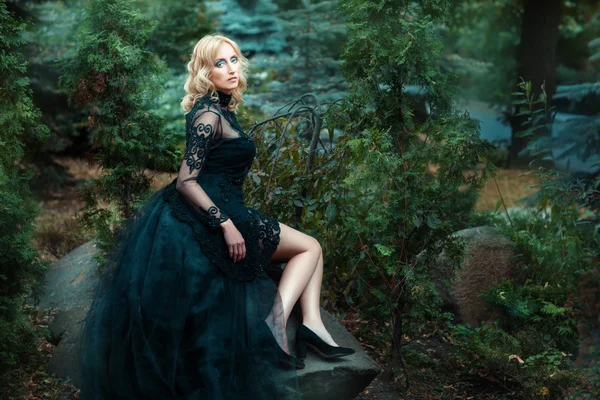 Mädchen schwarzes Kleid sitzt auf einem Felsen im Wald. — Stockfoto