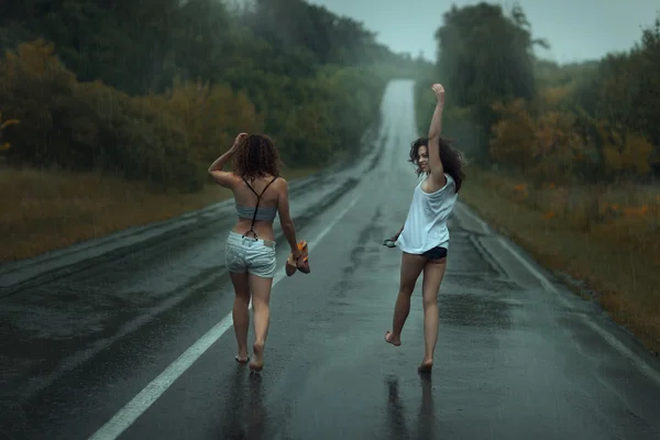 Dos chicas están en la carretera bajo la lluvia . —  Fotos de Stock