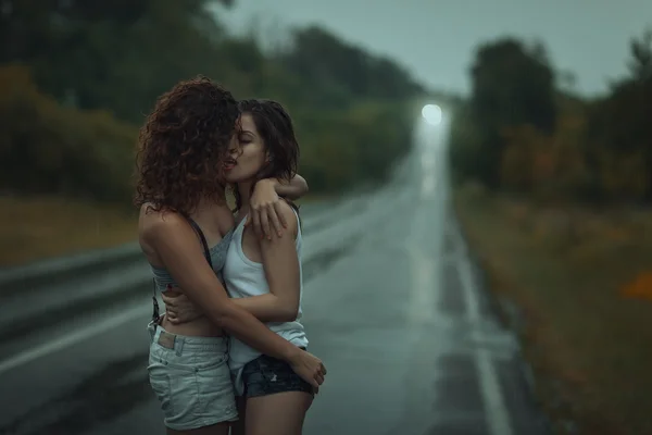 Lésbicas de meninas beijando debaixo de chuva pesada. — Fotografia de Stock