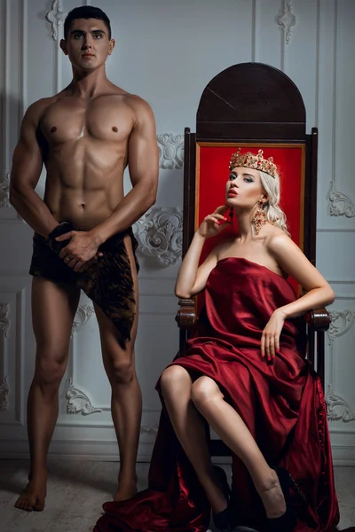 Queen sitting on a throne. Nearby is an athletic slave. — Stock Photo, Image