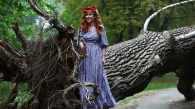 Kız bir çelenk ile düşmüş bir ağaç kökleri duruyor.