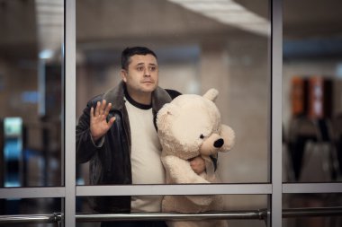 Man holding toy bear and looking sadly into the distance.