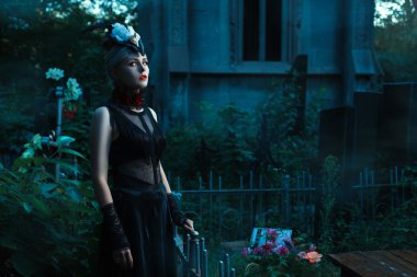 Woman with white eyes standing in a cemetery at night.