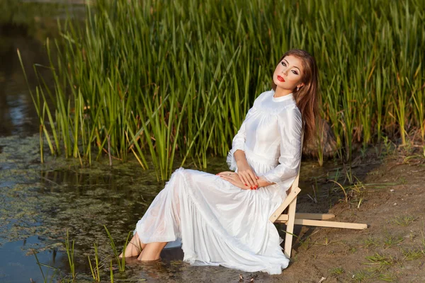 Beautiful girl sits on shore of the lake. — Stock Photo, Image