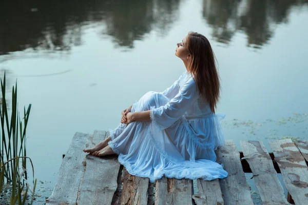 Girl sitting on a wooden pier and dreams. — Stock Photo, Image