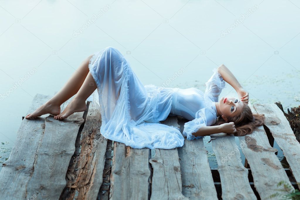 Gentle girl in white dress lying on a wooden pier.
