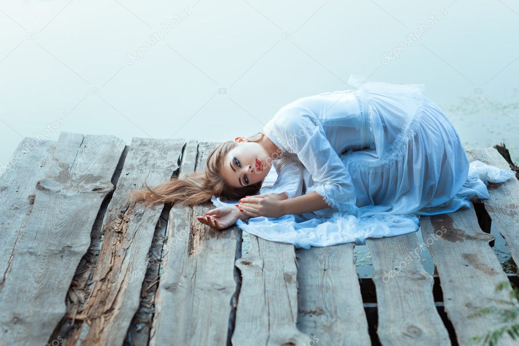 Beautiful girl with sad face lying on a wooden pier.