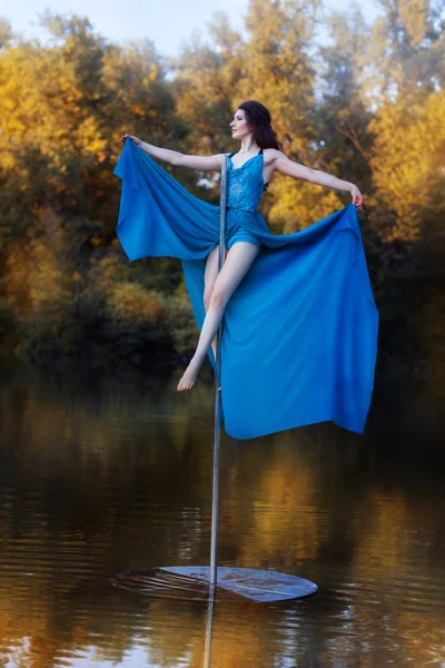 Girl in a blue dress sits high on pole dance. — Stock Photo, Image