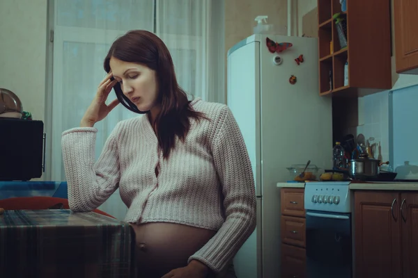 Femme enceinte triste assis dans la cuisine. Image En Vente