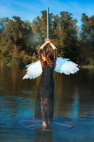 Flicka med ängel vingar står nära en poledance. — Stockfoto