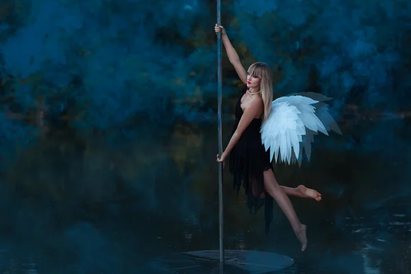 Fille avec ange ailes encerclant sur un pole dance . — Photo