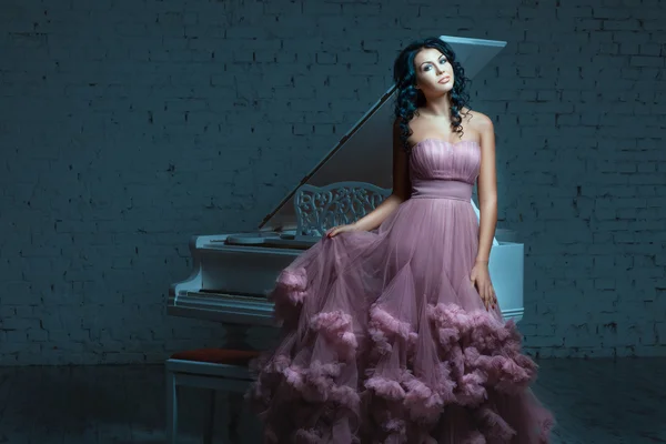 Hermosa mujer posando junto a un piano blanco . — Foto de Stock