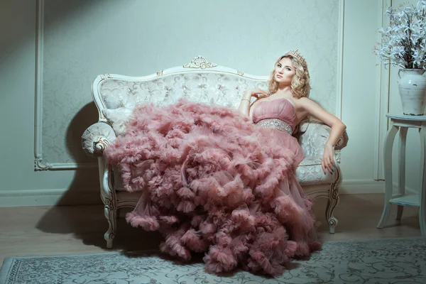 Flicka i en magnifik klänning sitter i soffan. — Stockfoto