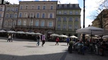 19 Nisan 2025. Krakow Polonya. Ziyaretçiler şehrin eski kentindeki ana meydanın kaldırımlı caddesinden geçiyorlar.