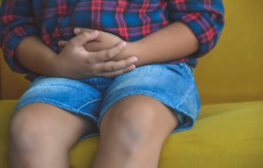 Karın ağrısı çeken Asyalı bir çocuk. Çocuk kanepede oturuyor, oturma odasındaki pencerelerin yanındaki bulantıdan muzdarip, ebeveyn bakımı, mide sorunları, sağlıklı konsept.. 