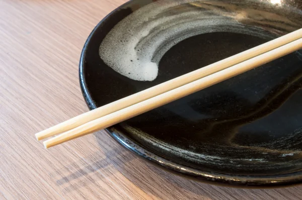 Chopsticks em uma tigela preta com fundo de madeira — Fotografia de Stock