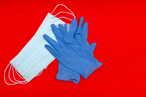 コロナウイルスから守る医療用マスク 赤い背景で 外科用保護マスク 青い手袋 — ストック写真
