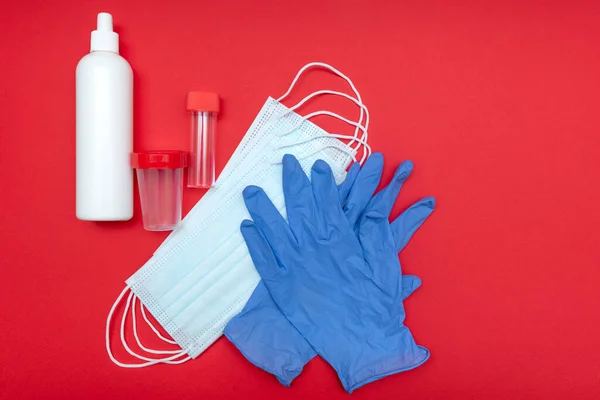 コロナウイルスから守る医療用マスク 赤い背景で 青い手袋 分析容器だ 接近中だ 消毒瓶 — ストック写真