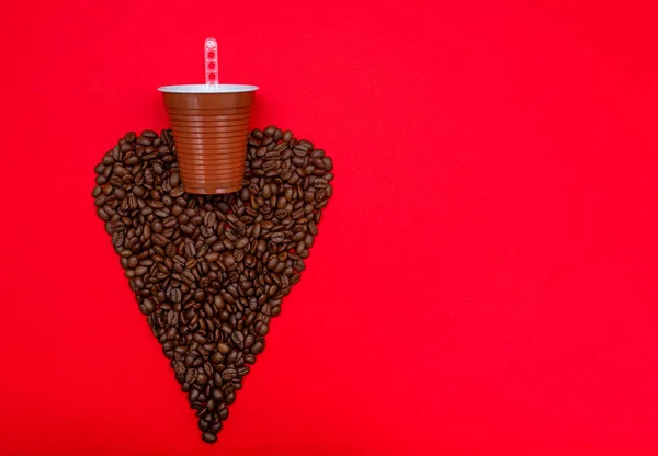 Black coffee grains in the form of a heart. A glass from a coffee machine. On a red background.