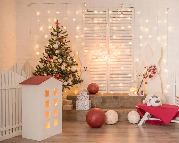 Children\'s New Year\'s decor in the studio. On a white brick wall there are lights, hares, a tree, red balls.