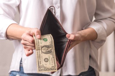 Beyaz gömlekli bir kadın eli, içinde para olan bir cüzdan tutuyor. Cüzdandaki son dolar..