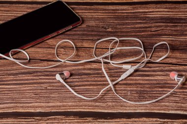 Telefon kahverengi arka planda. Telefonun beyaz kulaklıkları var. Yakın plan..