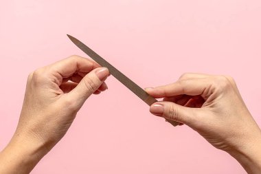 Pembe arka planda tırnaklarını kesen kadın eller. Yakın plan. Kız manikür yapıyor..