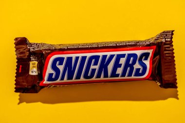 Packaging of chocolate in a brown wrapper with peanuts on a yellow background with a hard shadow. Close-up. View from above.
