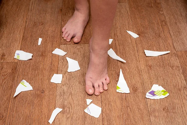 Children's feet are on the floor around the broken plate. The child broke the plate.