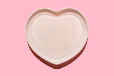 Kalp şeklinde plaka. Seramik sofra takımı. Pembe arka planda. Sert bir gölgeyle.