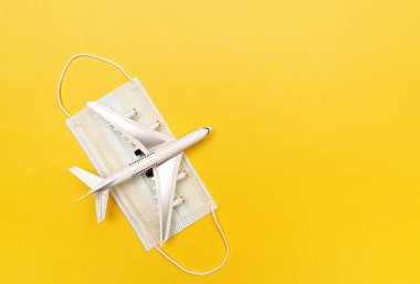 Beyaz uçak tıbbi koruyucu bir maskenin üzerinde yatıyor. Seyahat konsepti. Sarı arka planda.