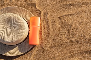 Orange bottle for sunscreen or lotion. Container with a black shadow on the sand. Summer hat. In summer on vacation.