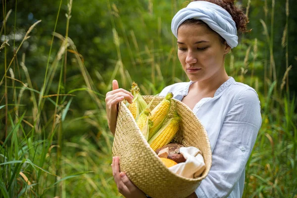 Farmer Girl kosárral kukorica cobs zöld, kenyér, tök és virágok. — Stock Fotó