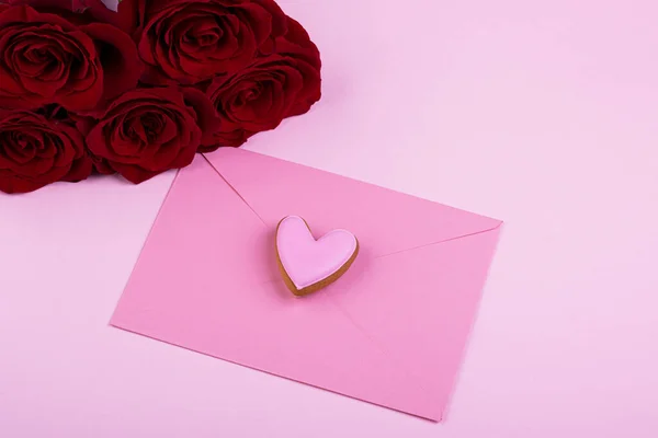 繊細なピンクの封筒とパステルピンクの背景にジンジャーブレッドの心を持つ赤いバラ 優しさ バレンタインデー 誕生日 母の日の概念 — ストック写真