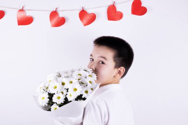Beyaz arka planda bir buket beyaz çiçekli çocuk. Arka planda kırmızı kalpler var. Sevgililer Günü konsepti, Anneler Günü