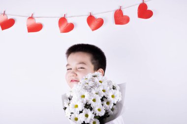 Beyaz arka planda bir buket beyaz çiçekli çocuk. Arka planda kırmızı kalpler var. Sevgililer Günü konsepti, Anneler Günü